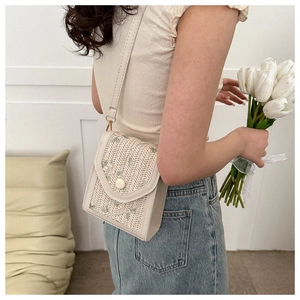 Detail of beige woven crossbody cell phone bag with leather strap on a female model