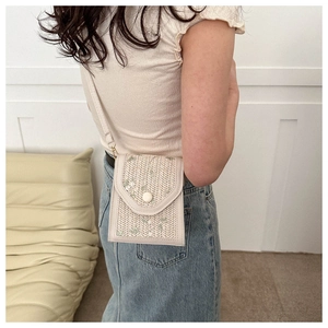Detail of woven phone bag featuring green floral embroidery and leather strap