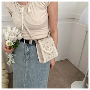 Detail of woven straw crossbody phone bag with floral patterns and a vintage leather trim