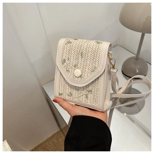 Close-up of woven straw cell phone bag featuring green floral embroidery and cream leather trim