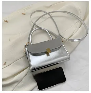 Silver metallic mini crossbody bag with top handle and gold clasp shown next to a phone