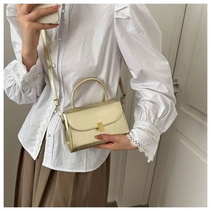 Detail of elegant gold crossbody bag with metallic finish and top handle on female model