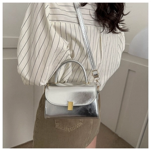 Detail of silver metallic crossbody bag with gold clasp shown on a model