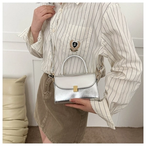 Detail of silver metallic crossbody bag with gold rectangular buckle on white wall