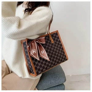 Detail of large tote bag with NK logo print and brown leather handles with silk scarf