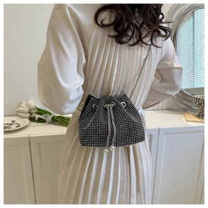 Detail of rhinestone bucket bag with pearl drawstrings worn by a model in a modern room