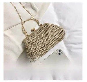 Detail view of a beige handmade straw bag with metal clasp and chain strap next to a phone