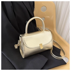 Detail of golden metallic crossbody bag with rectangular flap and rigid handle on black blazer