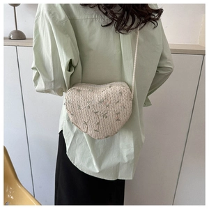Detailed embroidery of pink and green flowers on a heart-shaped woven straw crossbody bag
