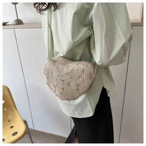 Detailed view of heart-shaped woven straw bag with floral embroidery and silver zipper