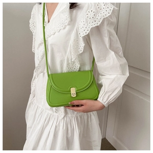 Detail of green leather saddle bag with gold metal clasp on white lace dress