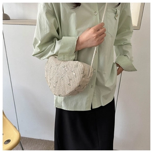 Detailed shot of beige heart-shaped woven bag with floral embroidery and braided strap