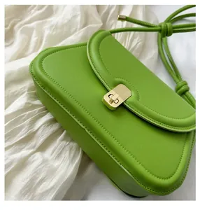 Detailed close-up of fruit green saddle bag featuring a gold buckle and knotted strap