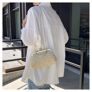 Detail of hand-woven straw crossbody bag with gold metal frame and chain strap