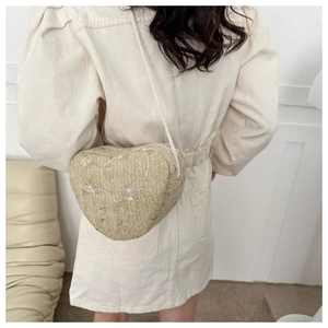 Detail of heart-shaped woven straw bag with floral embroidery and crossbody strap