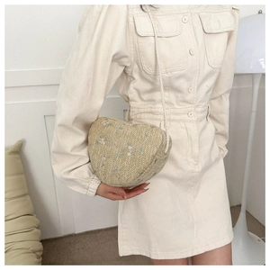 Detail of heart-shaped woven straw bag with floral embroidery worn as crossbody