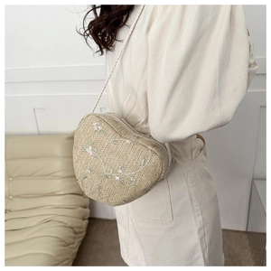 Detail of heart-shaped straw crossbody bag with floral embroidery and woven strap