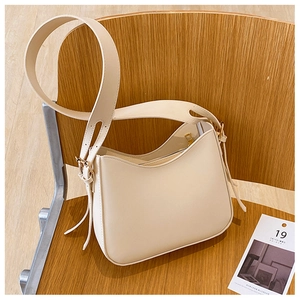 Détail d'un sac à bandoulière demi-lune crème avec large sangle en cuir sur une chaise