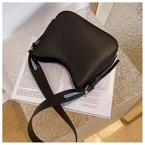Détail du sac hobo en cuir noir avec ferrures dorées posé sur un livre esthétique