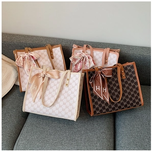 Close-up of stylish monogram tote bags with silk scarves on a soft fabric sofa