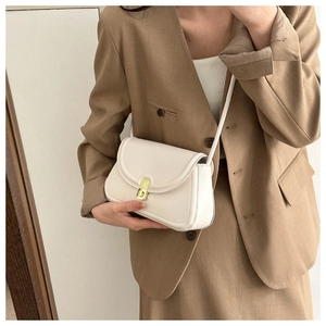 Detail of white leather saddle bag with gold metal lock on khaki blazer outfit