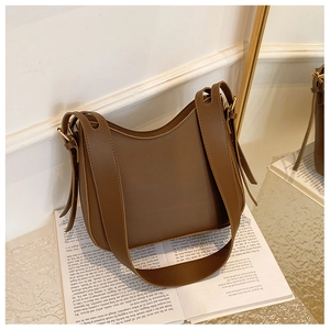 Détail d'un sac bandoulière marron en cuir avec boucle dorée posé sur un livre ouvert