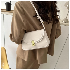 French style cream leather saddle bag with gold clasp shown on a shoulder in brown suit