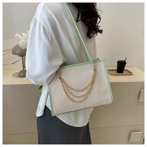 Detail of light green straw tote bag featuring decorative gold chains and spacious design
