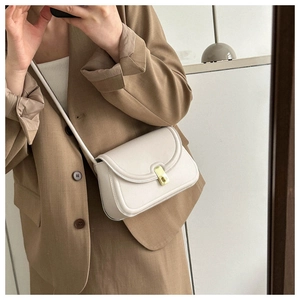 Detail of a cream faux leather saddle bag with gold buckle on a khaki blazer outfit