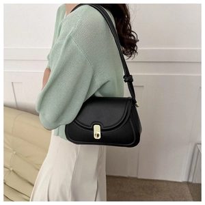 Side view of black leather saddle bag with gold buckle worn on shoulder over green top