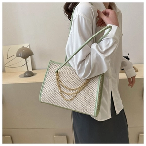 Close-up of a large woven straw tote with green leather trim and golden chains