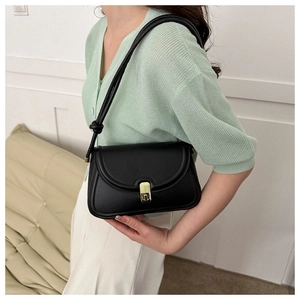 Side view of black faux leather saddle bag with gold lock and knot strap detail