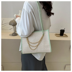 Detail of a large straw tote bag with green leather trim and golden chain decoration