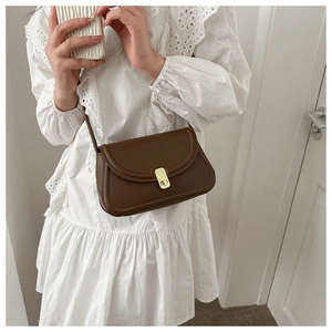 Close-up of brown saddle crossbody bag with gold twist-lock on white lace dress