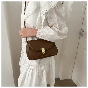 Detail of vintage dark brown leather saddle bag with gold buckle on white lace dress