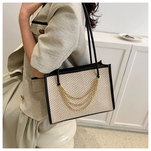 Close-up of beige woven tote bag with black leather trim and golden chain details