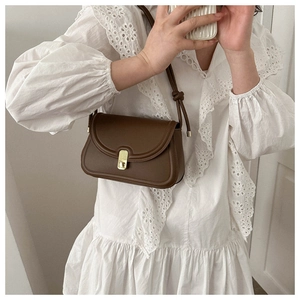 Detail of vintage dark brown saddle bag with golden clasp worn by a woman in white lace