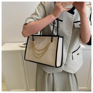 Detail of hand-woven straw tote bag with black trim and elegant gold chain tassels