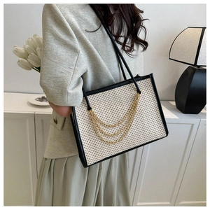 Detail of a beige woven tote bag with three-layer gold chain and black leather trim