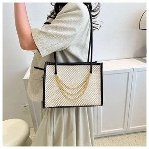 Detail view of large straw tote bag with black leather trim and decorative gold chain tassels
