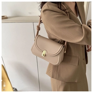 Detail of a beige leather saddle bag featuring a gold square clasp and knotted shoulder strap
