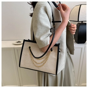 Detail of woven straw tote bag with black leather trim and layered gold chain accents