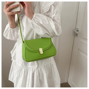 Close-up of bright green saddle bag with gold swivel lock on white lace dress