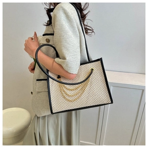 Detail of contrast stitching straw tote bag featuring decorative gold chains and strap