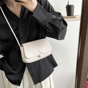 Close-up of a cream leather square crossbody bag with a round gold buckle on a model