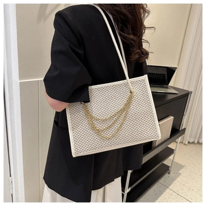 Detail of a beige woven tote bag with white trim and triple gold chain decoration