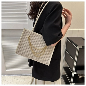 Detail of woven tote bag with houndstooth texture and stylish triple gold chain accents