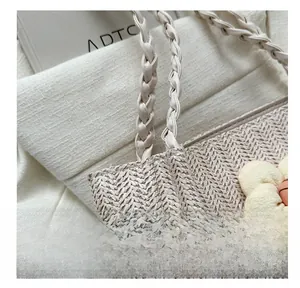 Détail du sac cabas en paille beige avec anses tressées et pendentif fleur jaune