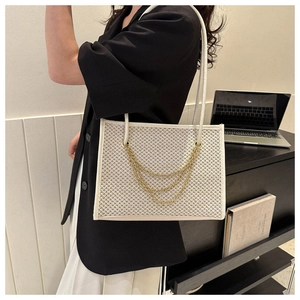 Detail of cream woven tote bag with three-tier gold chain accents in an office setting