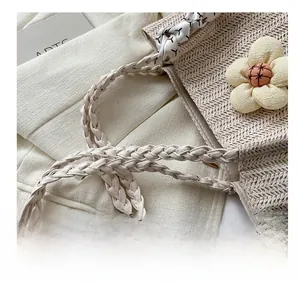 Détail de la poignée en corde tressée et de la fleur crème sur un sac cabas en paille